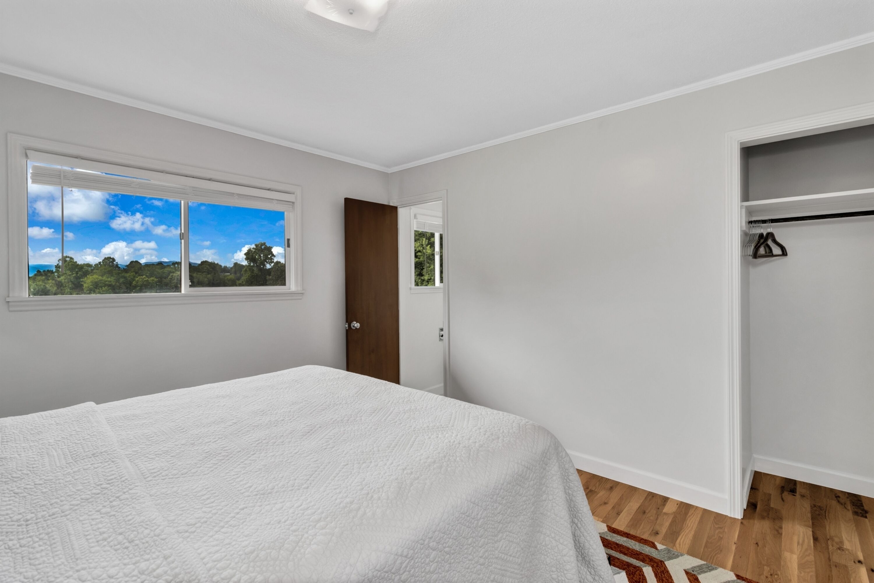 A bedroom with a large bed, a wardrobe, and a window with a view of trees.