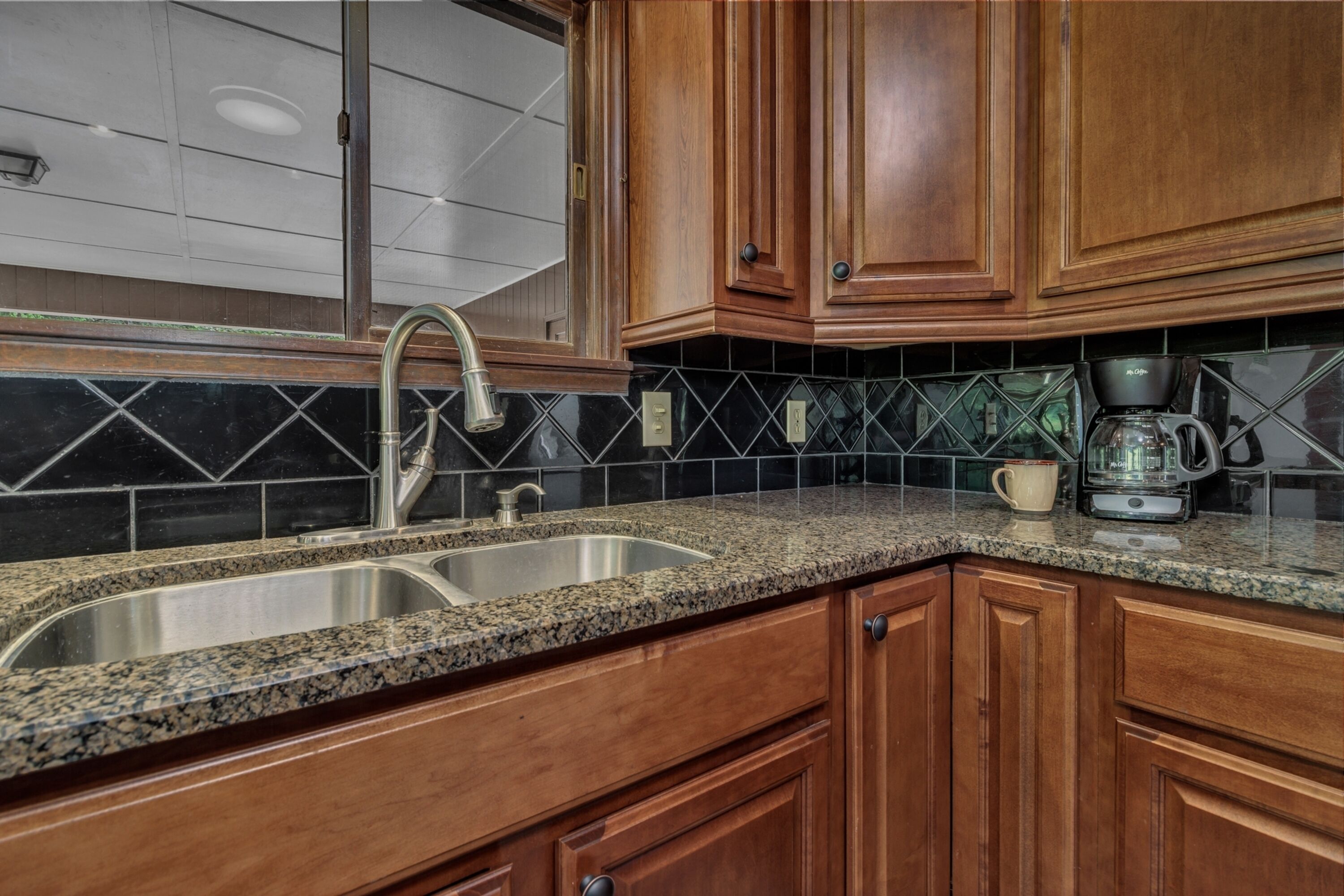 A kitchen with granite countertops, wooden cabinets, a stainless steel sink, and a coffee maker.