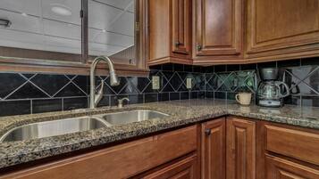 A kitchen with granite countertops, wooden cabinets, a stainless steel sink, and a coffee maker.