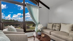 Ein Wohnzimmer mit großem Fenster, einer Couch, einem Sessel und einem Couchtisch.