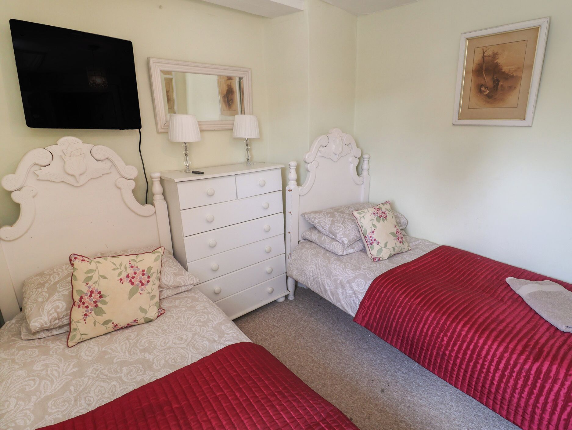A bedroom with two beds, a dresser, a mirror, and a painting on the wall.