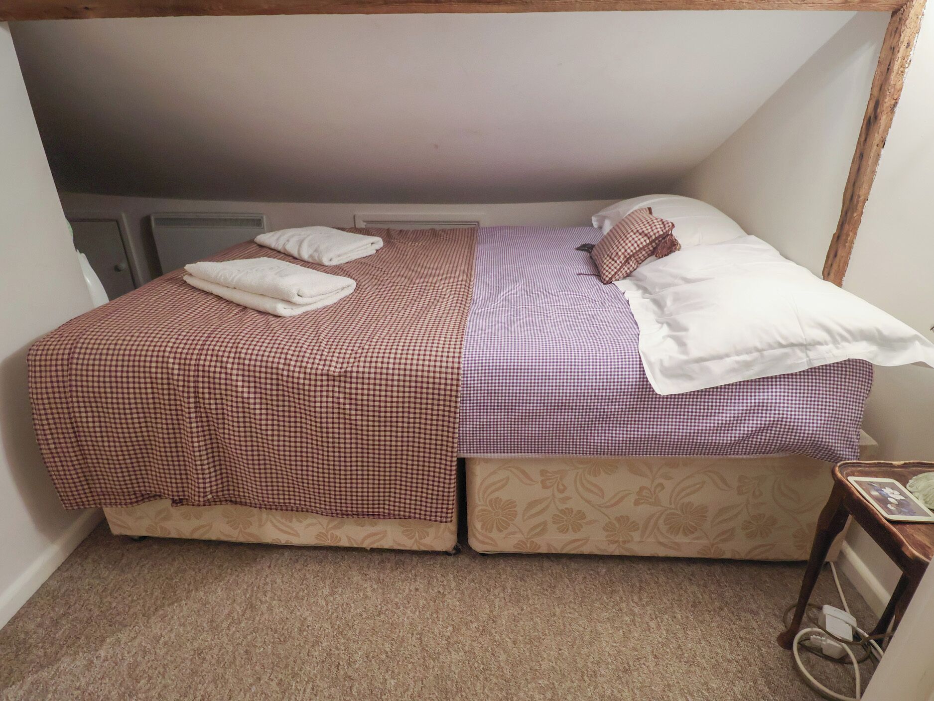 A bedroom with a bed, two pillows, a blanket, and a bedside table with a lamp.