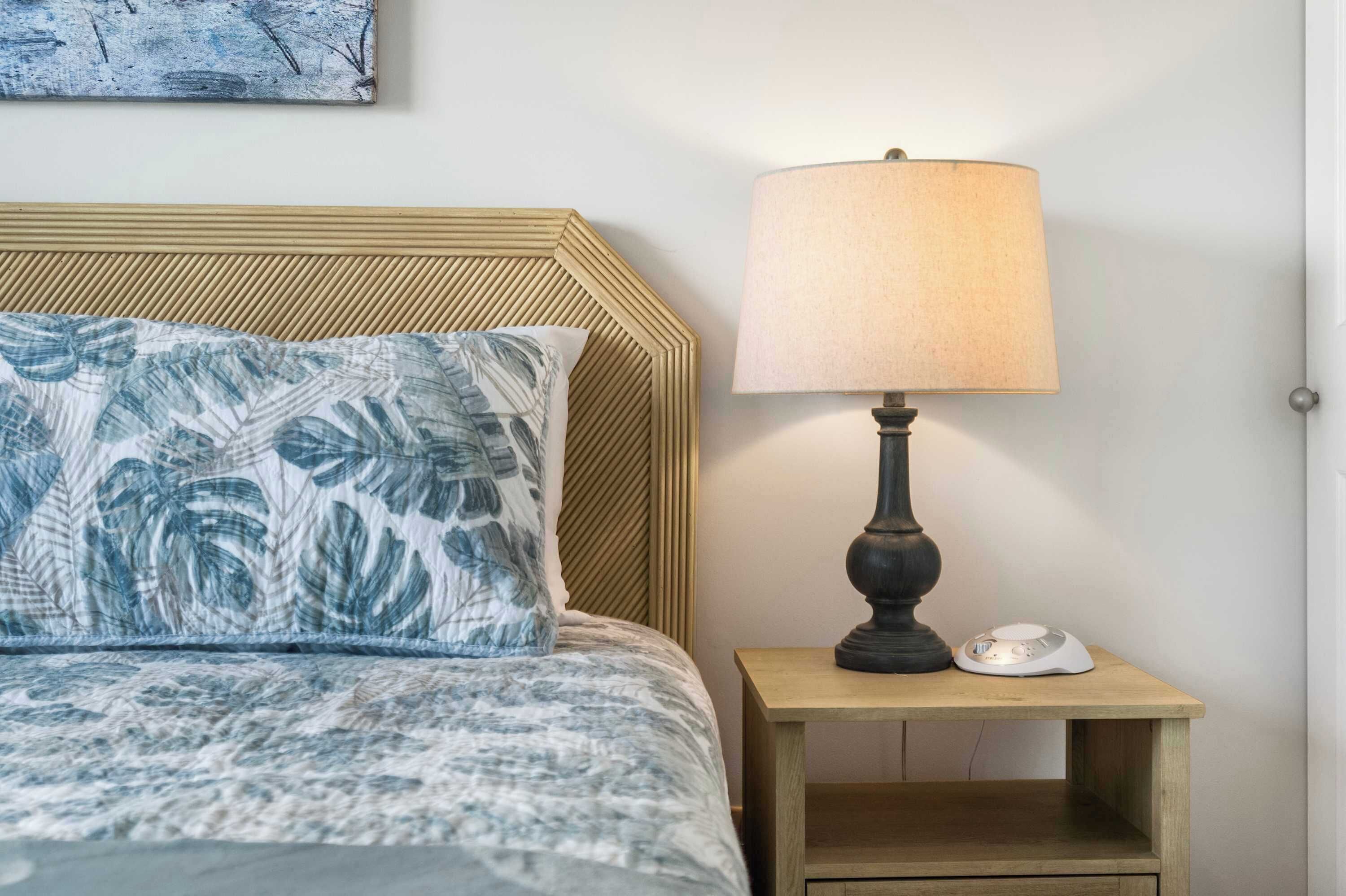 A bed with a patterned pillow, a bedside lamp, and a small table with a device on it.