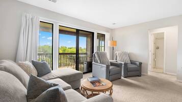 A spacious living room with a large sofa, two armchairs, a coffee table, and a view of a balcony with outdoor furniture.