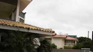 A residential area with a house featuring a tiled roof, a balcony, and a satellite dish. There are palm trees and a gravel pathway. - Pousada Aloha Mariscal (Bombinhas)