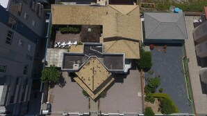 An aerial view of a residential building with a rooftop terrace, a small garden, and a parking area. - Pousada Aloha Mariscal (Bombinhas)