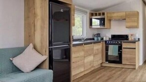 A compact kitchen with wooden cabinets, a built-in microwave, and a stove. - River Meadows Retreat. Contemporary, spacious caravan. 3 Bedroom, sleeps 8 (Great Billing)
