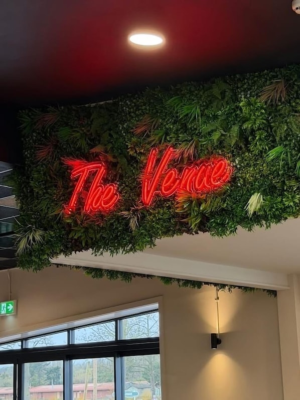 A neon sign with 'The Venue' in red, surrounded by green foliage.