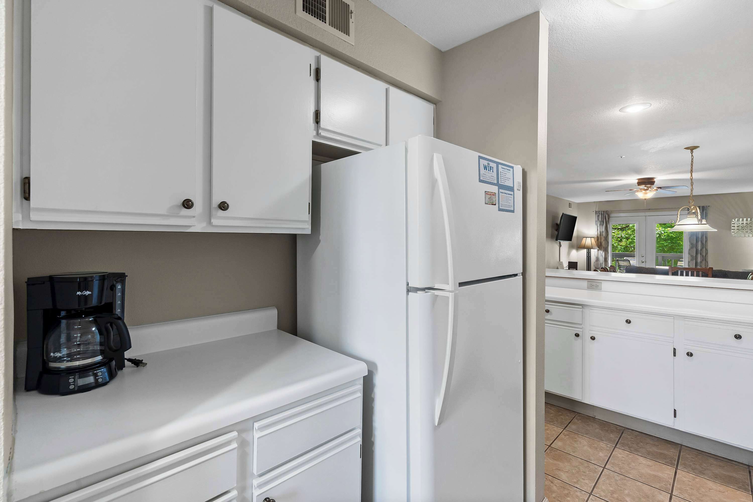 A kitchen with white cabinets, a white refrigerator, and a black coffee maker on the counter.