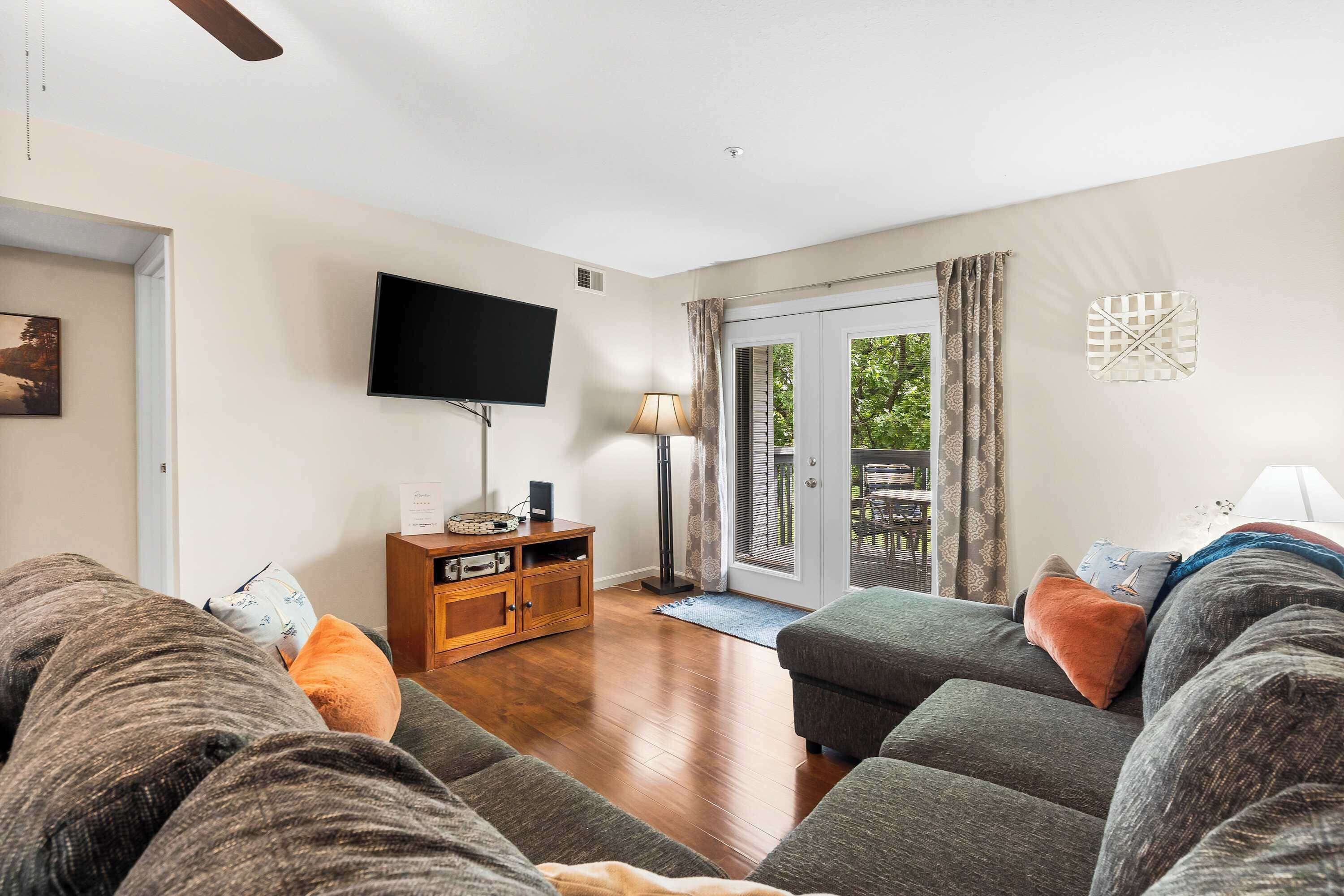 A living room with a sofa, a television, a wooden cabinet, and a sliding glass door leading to an outdoor area.