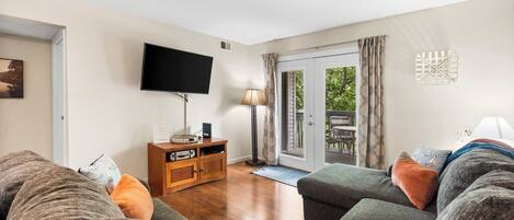 A living room with a sofa, a television, a wooden cabinet, and a sliding glass door leading to an outdoor area.