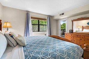 A bedroom with a bed, a dresser, a window with curtains, and a view of greenery outside.