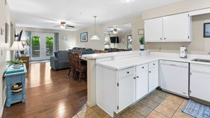 A modern kitchen with white cabinets, a dishwasher, and a dining area with a gray sofa and wooden chairs. - Ron's Retreat Stay for 6 With Resort Amenities (Branson)
