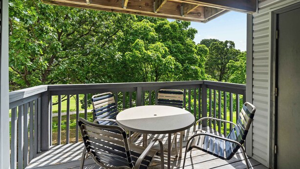 A wooden deck with a round table and metal chairs, overlooking a lush green landscape. - Ron's Retreat Stay for 6 With Resort Amenities (Branson)