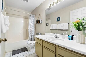 A modern bathroom with a bathtub, toilet, and sink. There is a shower curtain, a towel rack, and a mirror.