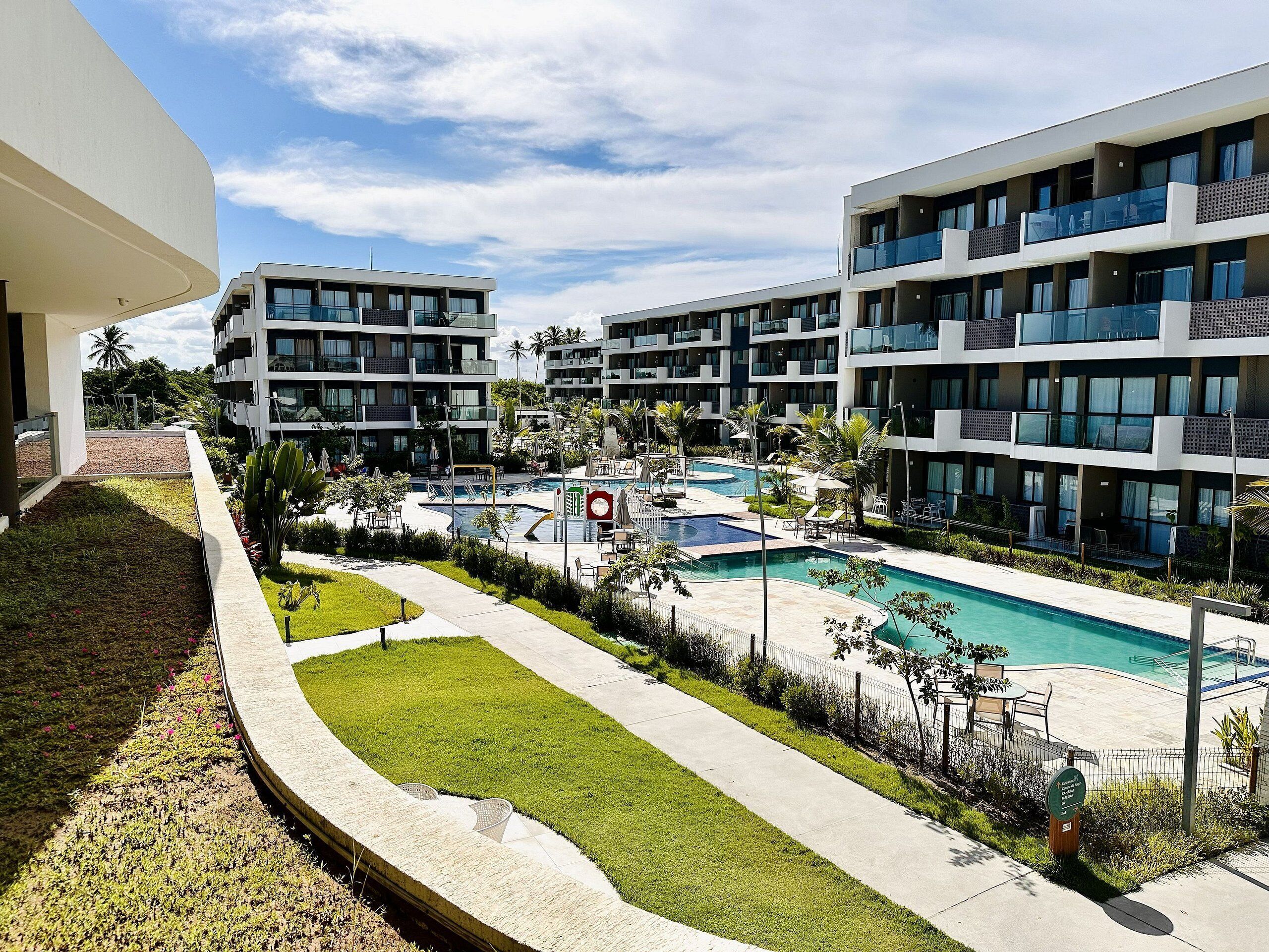 Un hotel moderno con varios balcones, una piscina central y un jardín bien cuidado.