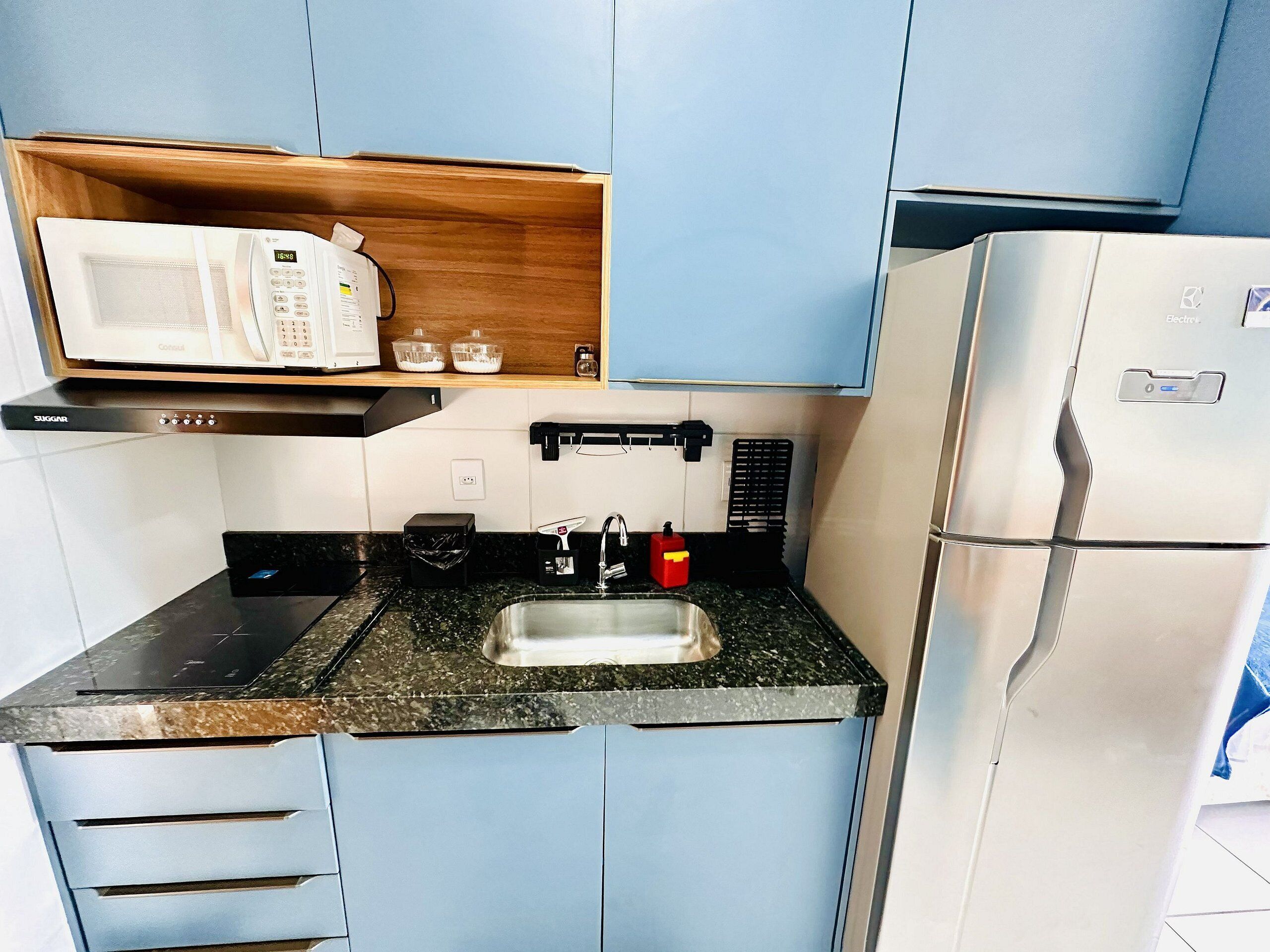 Una cucina compatta con forno a microonde, lavello e frigorifero.