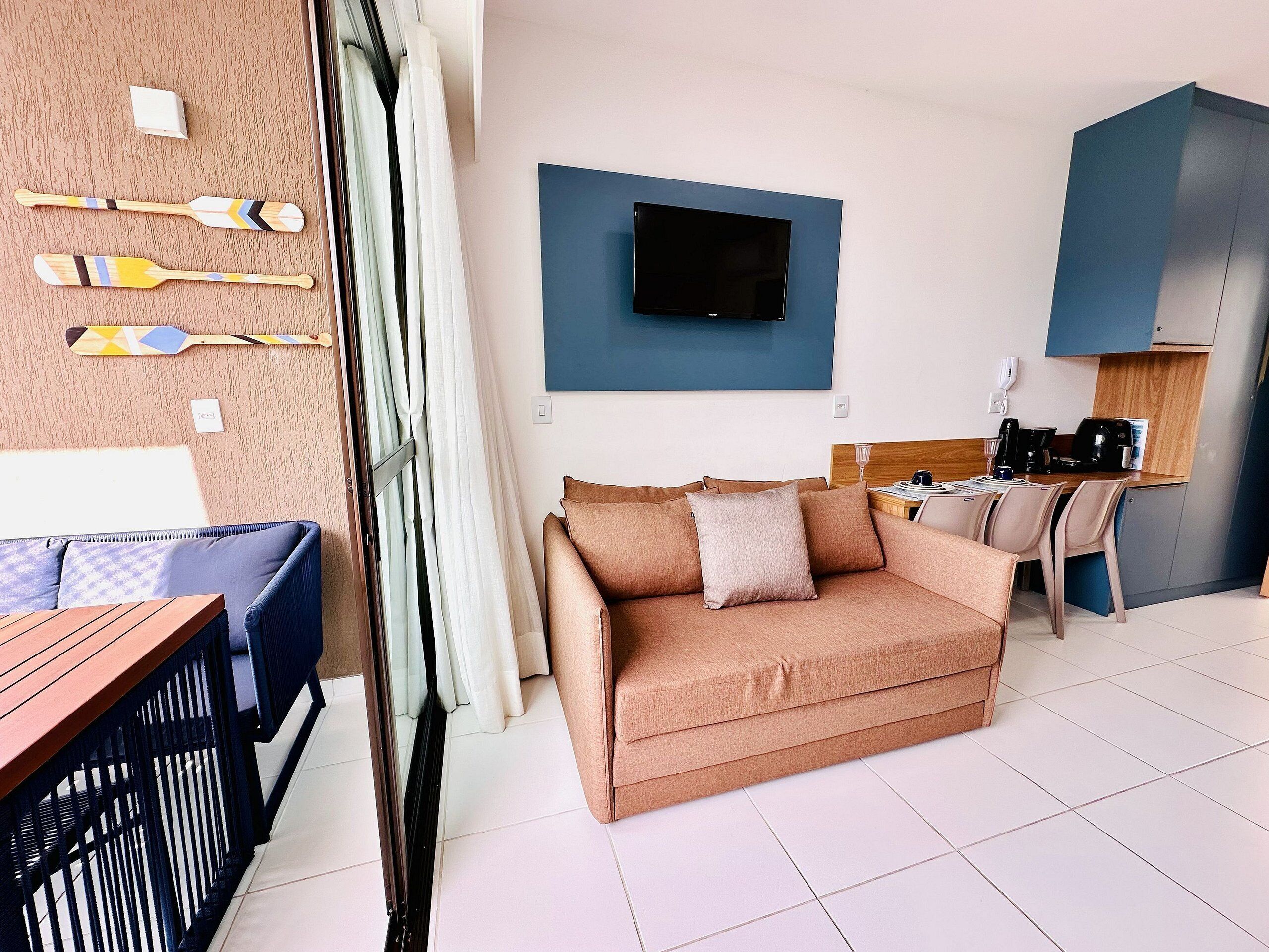 Ein modernes Zimmer mit einer Couch, einem Esstisch, einem an der Wand befestigten Fernseher und einer Küchenzeile.