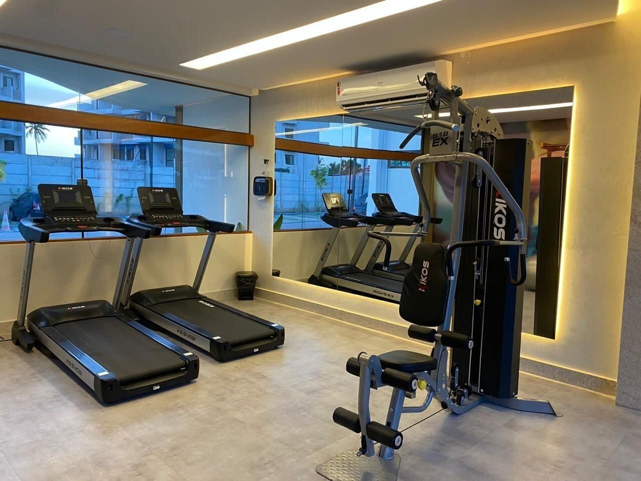 Un gimnasio con cintas de correr, máquinas de pesas y un amplio ventanal con vistas a edificios.