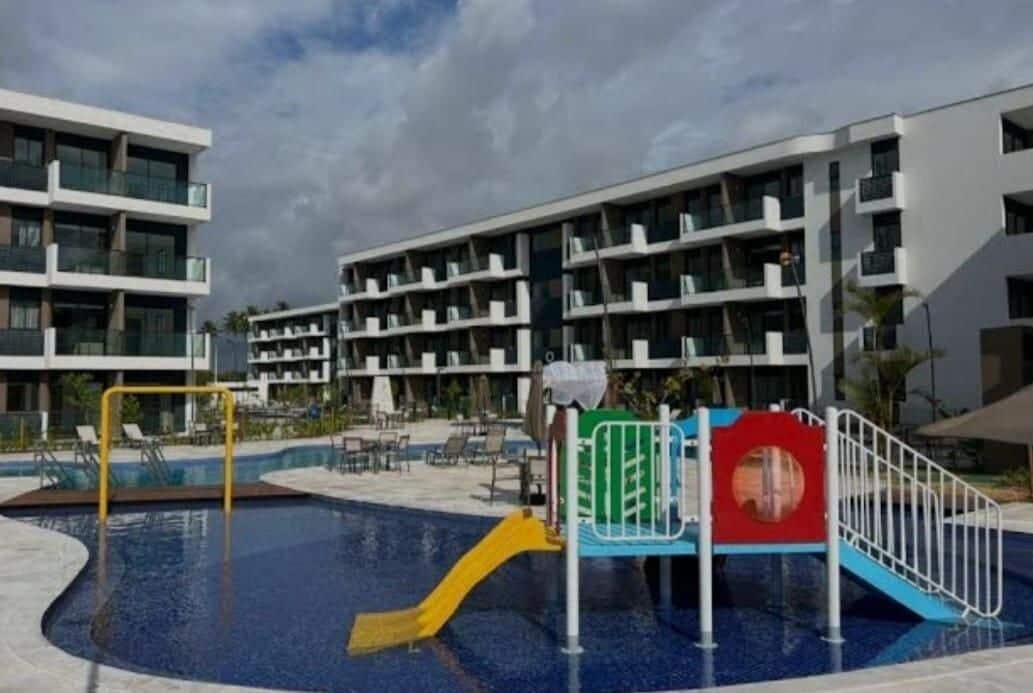 A swimming pool with a slide, surrounded by modern buildings with balconies.