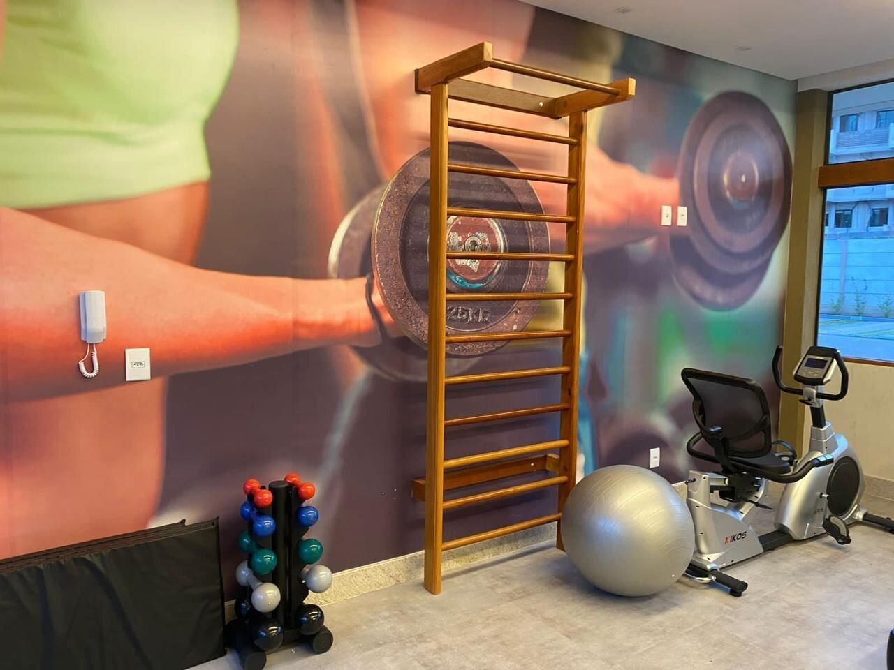 A gym with exercise equipment, a wall-mounted phone, and a window with a view.
