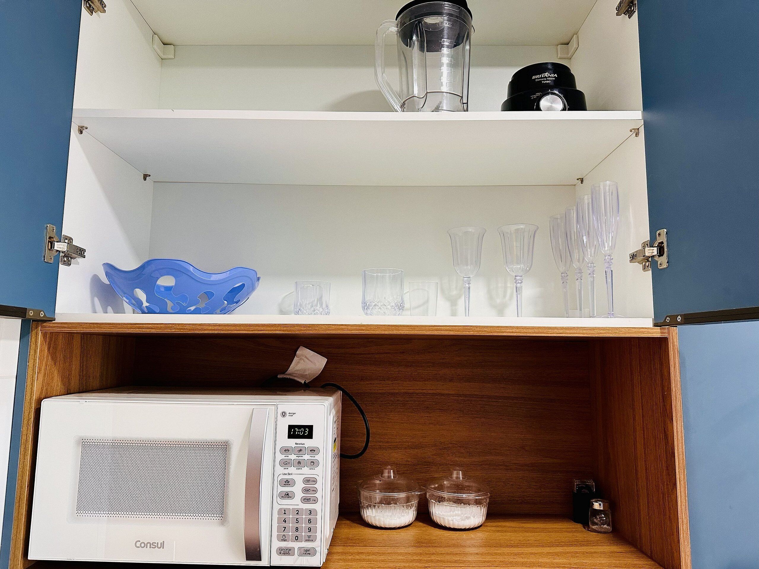 Una cocina con microondas, licuadora y varios vasos en estantes.