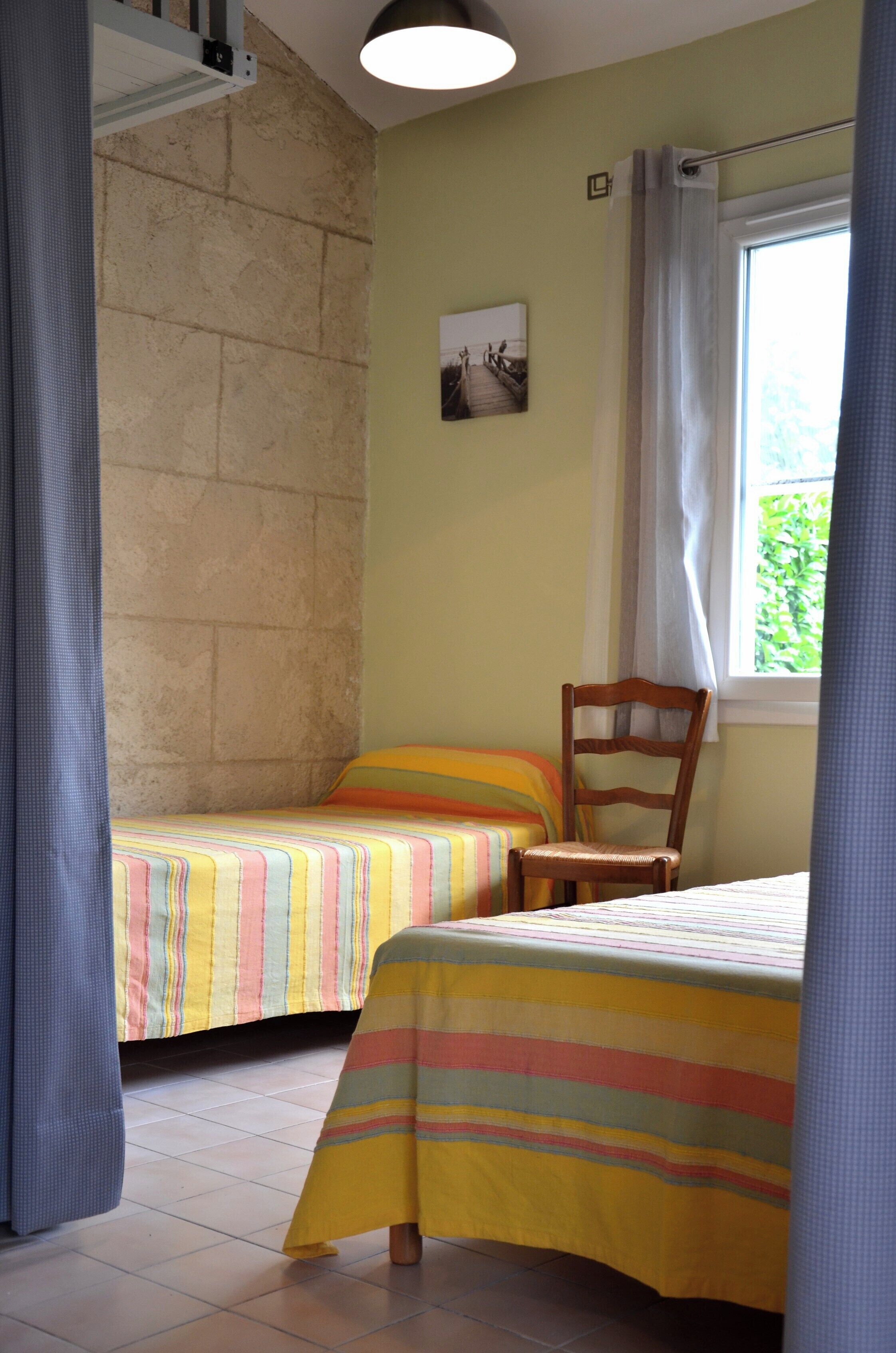 Quarto com duas camas, uma cadeira, janela com cortinas e um quadro na parede.