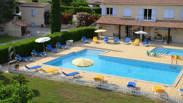 Une piscine entourée d’une clôture blanche, avec des chaises longues et des parasols.