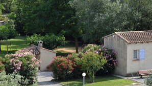 Une allée de gravier mène à une maison dotée d’un petit jardin et d’un banc.