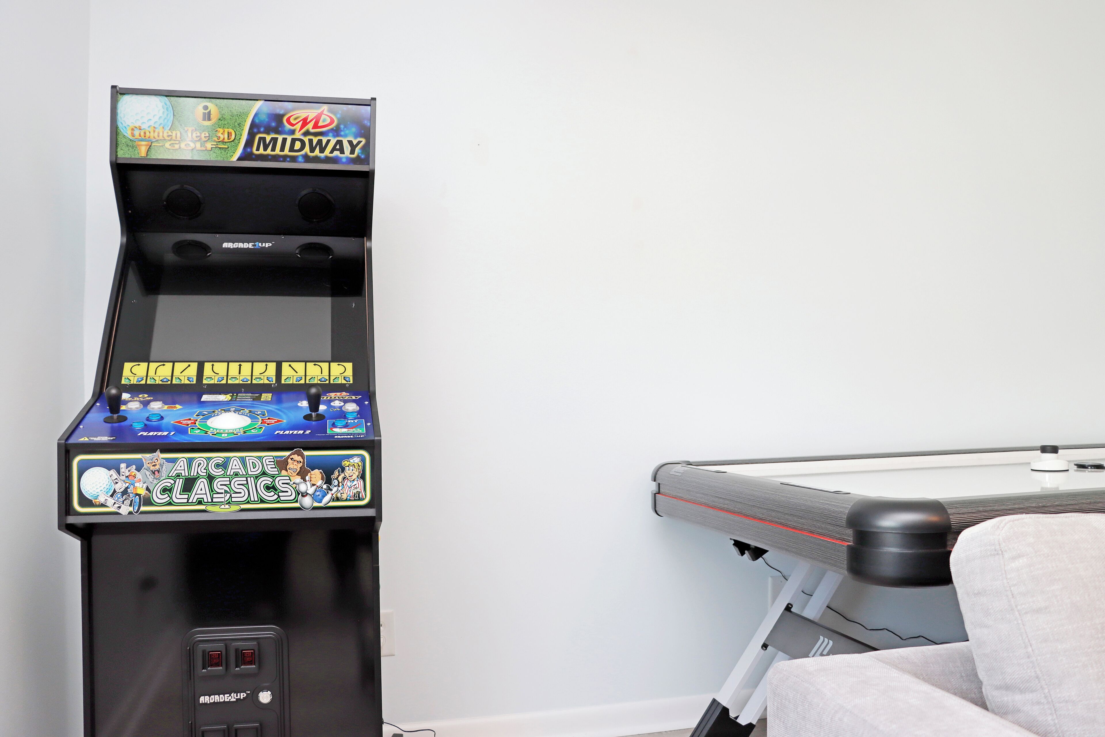 A gaming arcade machine with a screen and control panel, next to a massage table.
