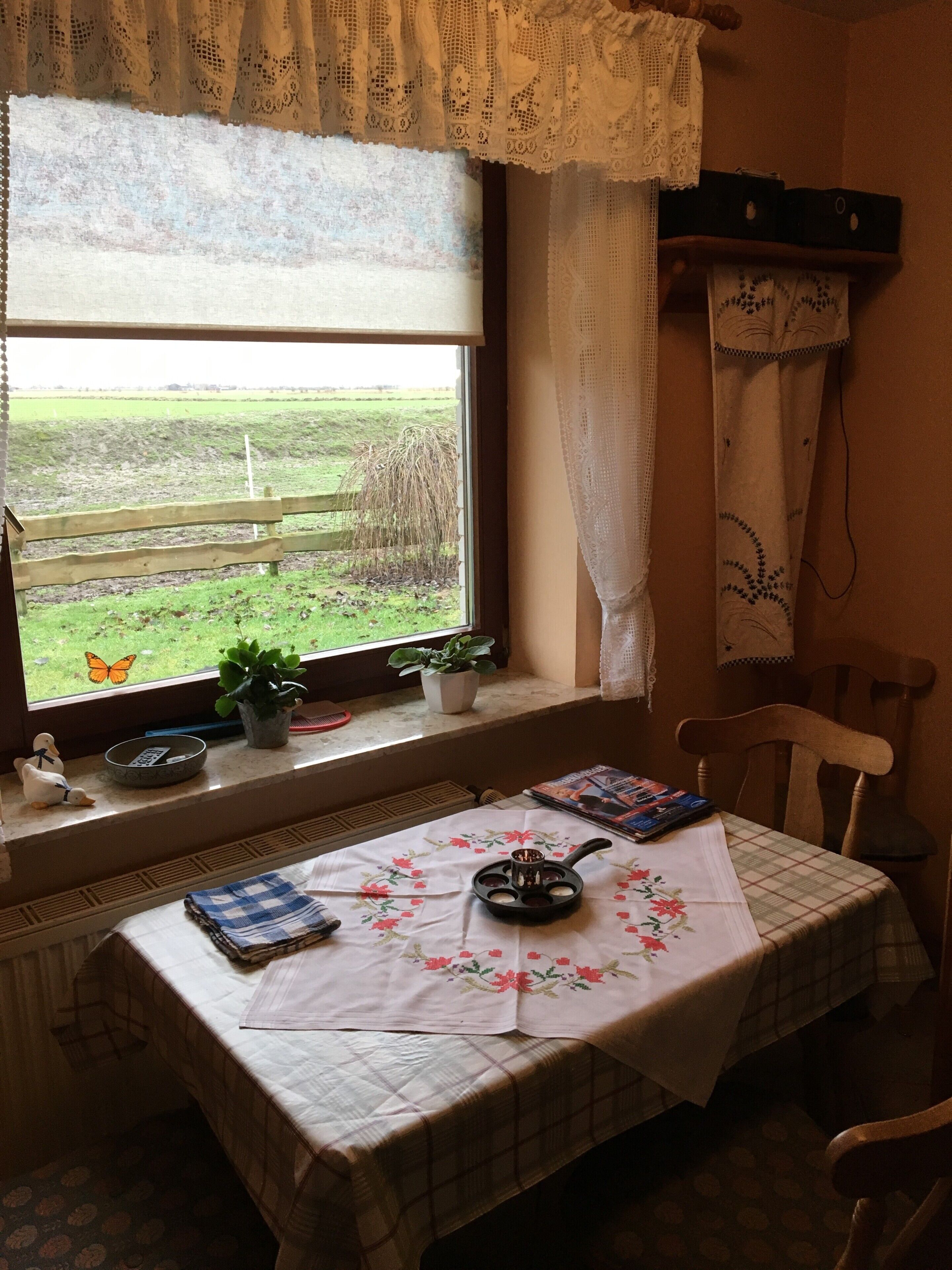 A room with a table set for tea, a window with a view of a field, and a chair.