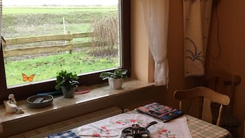 A room with a table set for tea, a window with a view of a field, and a chair.