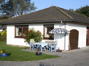 Une maison avec un toit en tuiles, une porte d’entrée et un petit porche avec une table et des chaises.