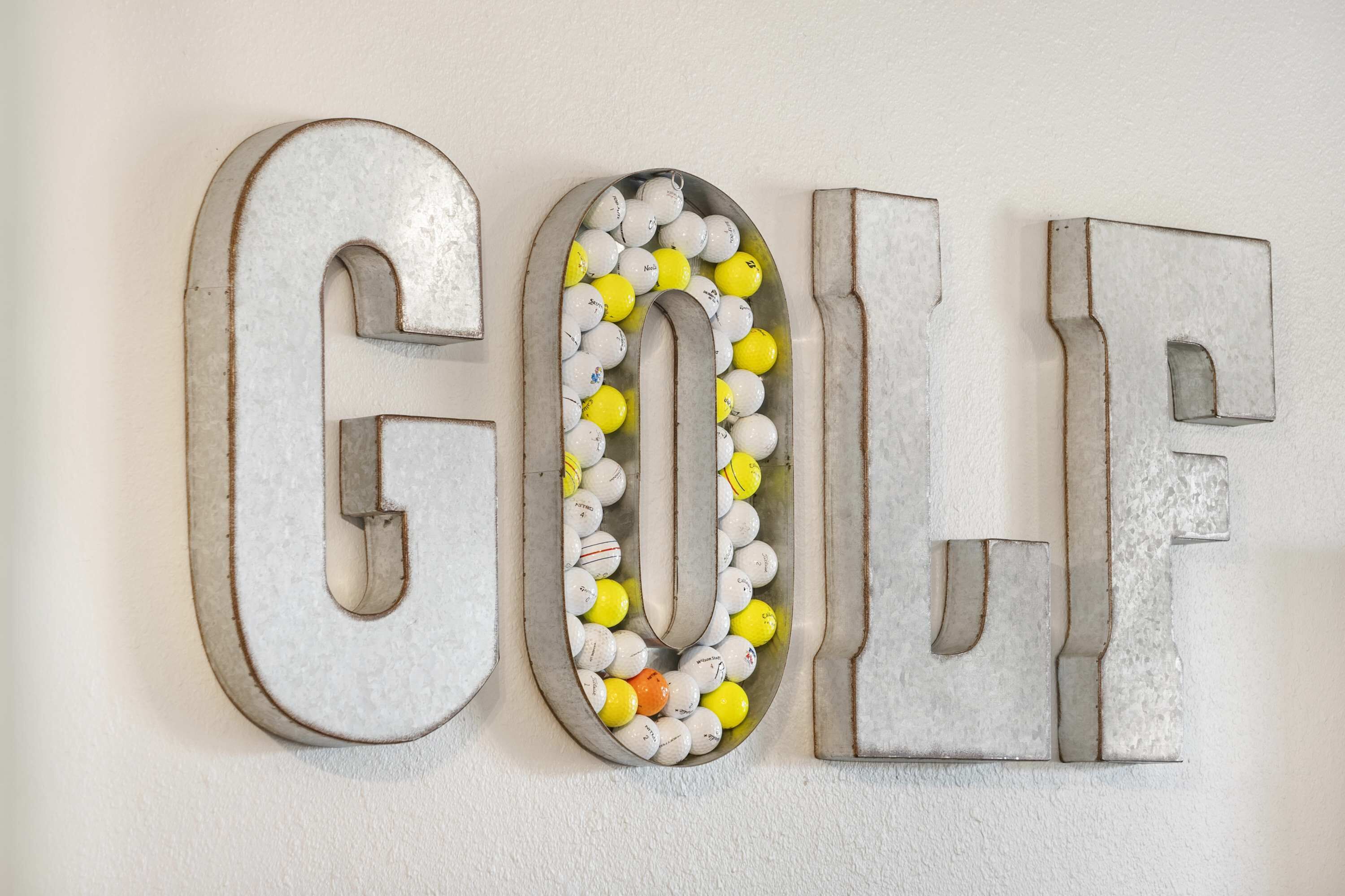 Un mur sur lequel le mot « GOLF » est écrit en grandes lettres métalliques, et des balles de golf sont disposées à l’intérieur des lettres.