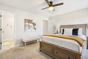 A bedroom with a bed, a bench, a ceiling fan, and a door. - Royale Tee Retreat - Golf Dream (Branson)