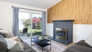 Una sala de estar moderna con chimenea, un sofá, una mesa de centro y un ventanal corredizo que da a un jardín.