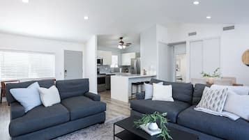 A modern living room with two grey sofas, a black coffee table, and a kitchen in the background.