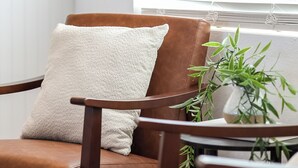 Un sillón de cuero marrón con un cojín texturizado, colocado junto a una mesita con una planta en maceta.