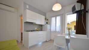 A compact kitchen with white cabinets, a dining area with a white table and chairs, and a window with curtains. - Cozy holiday flat in a quiet area (Bibione)