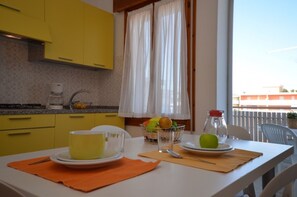 Un coin repas avec une table dressée pour deux personnes, comprenant une tasse jaune, un verre, une assiette avec une pomme et un panier de fruits.