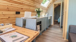Une chambre confortable, aménagée dans le style d’un chalet, avec un plafond en bois, une table à manger agrémentée d’un panneau d’accueil, un coin cuisine et une vue dégagée sur l’extérieur grâce à une porte ouverte.