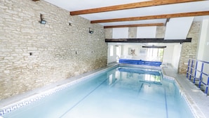 Une piscine avec des murs en pierre et des poutres en bois, un bord de piscine bleu et une barrière de sécurité bleue.