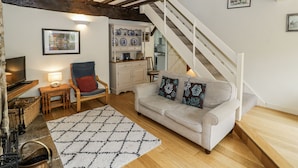 Un salon confortable avec un canapé, un téléviseur, une chaise en bois, une petite table avec une lampe et un escalier menant à un étage supérieur.