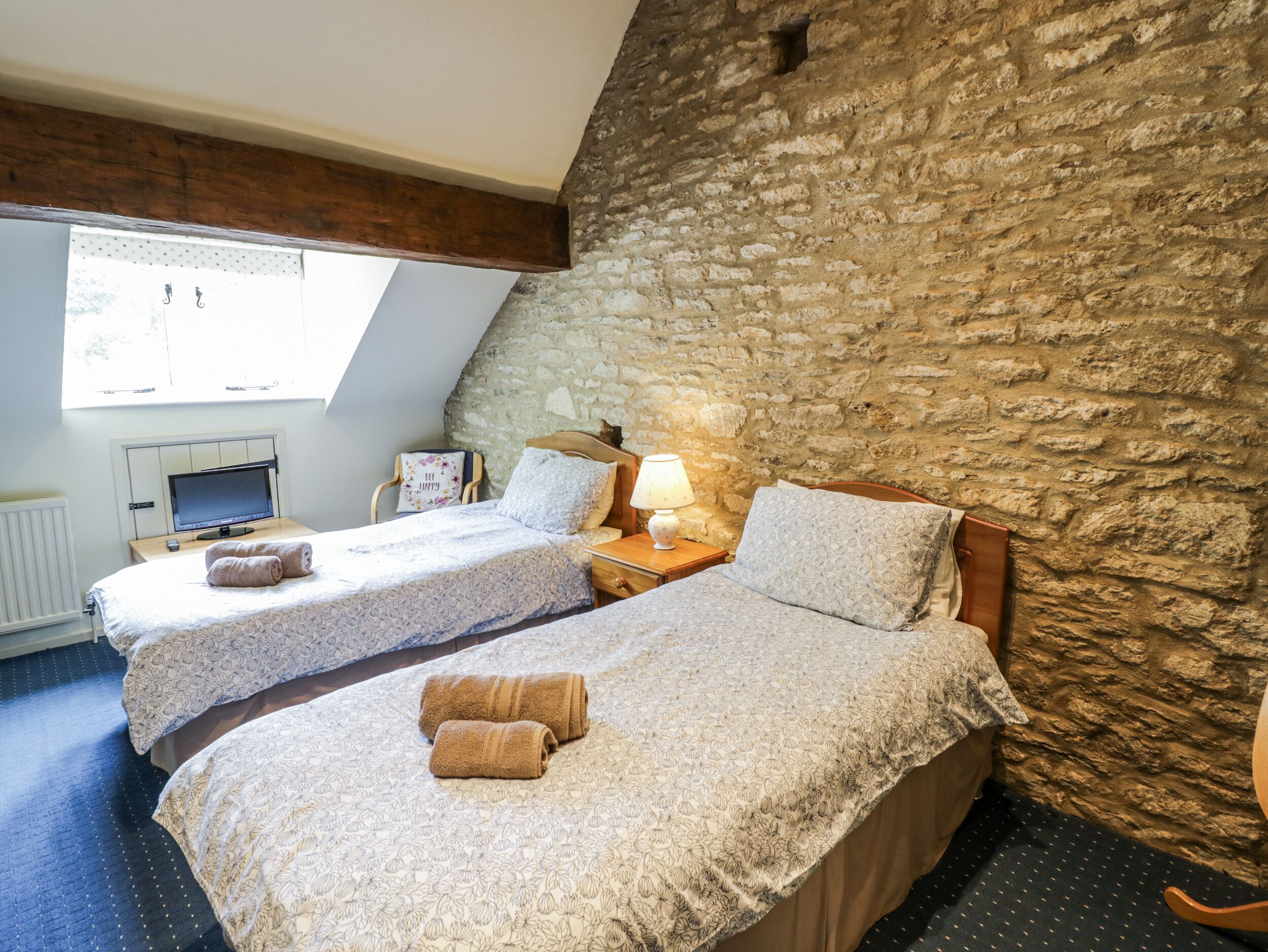 Un dormitorio con dos camas, una pared de piedra, un televisor y una ventana.