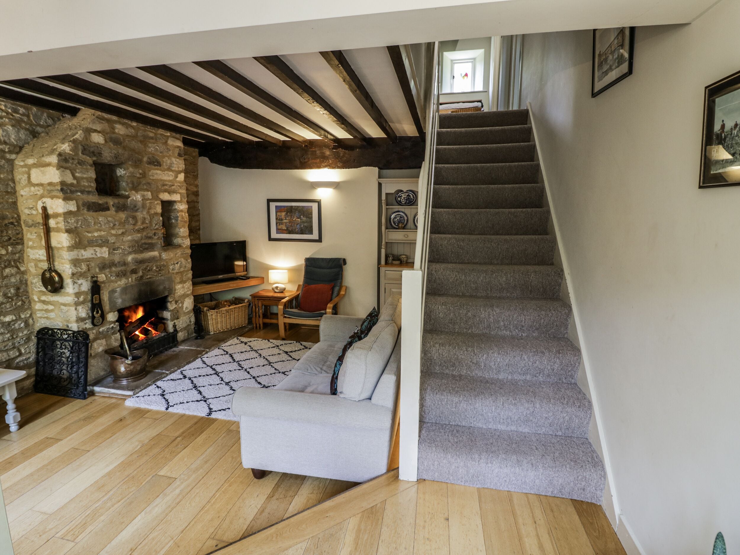 A cozy living room with a stone fireplace, a comfortable sofa, a TV, and a staircase.