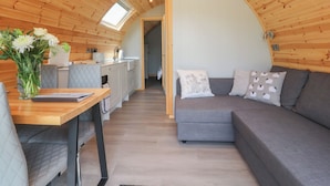 Un intérieur de chalet chaleureux comprenant un coin repas, une kitchenette et un espace de vie incurvé avec un canapé et des coussins.