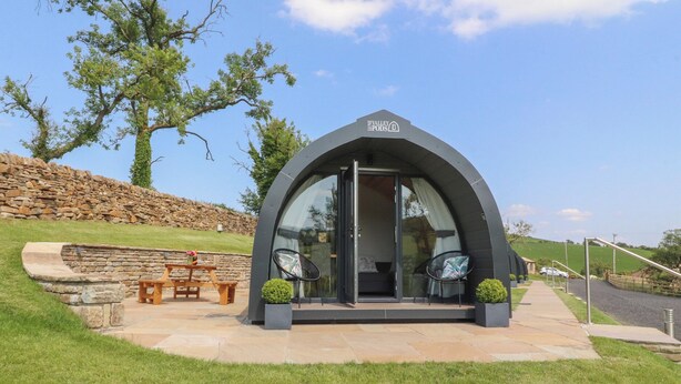Une structure moderne à arc, dotée d’une porte en verre, d’un mur en pierre et d’un banc.