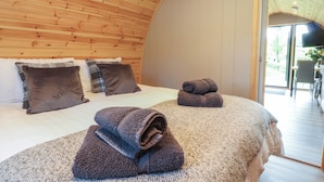 Une chambre confortable avec un plafond en bois aux lignes courbes, un grand lit agrémenté de nombreux coussins et des serviettes soigneusement pliées posées sur un tapis à motifs.