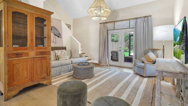 A spacious living room with a wooden cabinet, a sofa, a round ottoman, a clear table, and a large window with curtains.