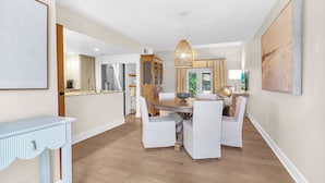A modern kitchen with white cabinetry, a dining area with a round table and white chairs, and a hanging light fixture.